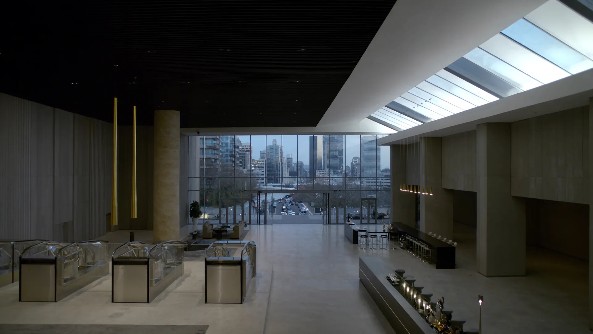 Modern urban hotel lobby with floor-to-ceiling glass windows overlooking a city skyline at dusk, polished concrete and brass interior details