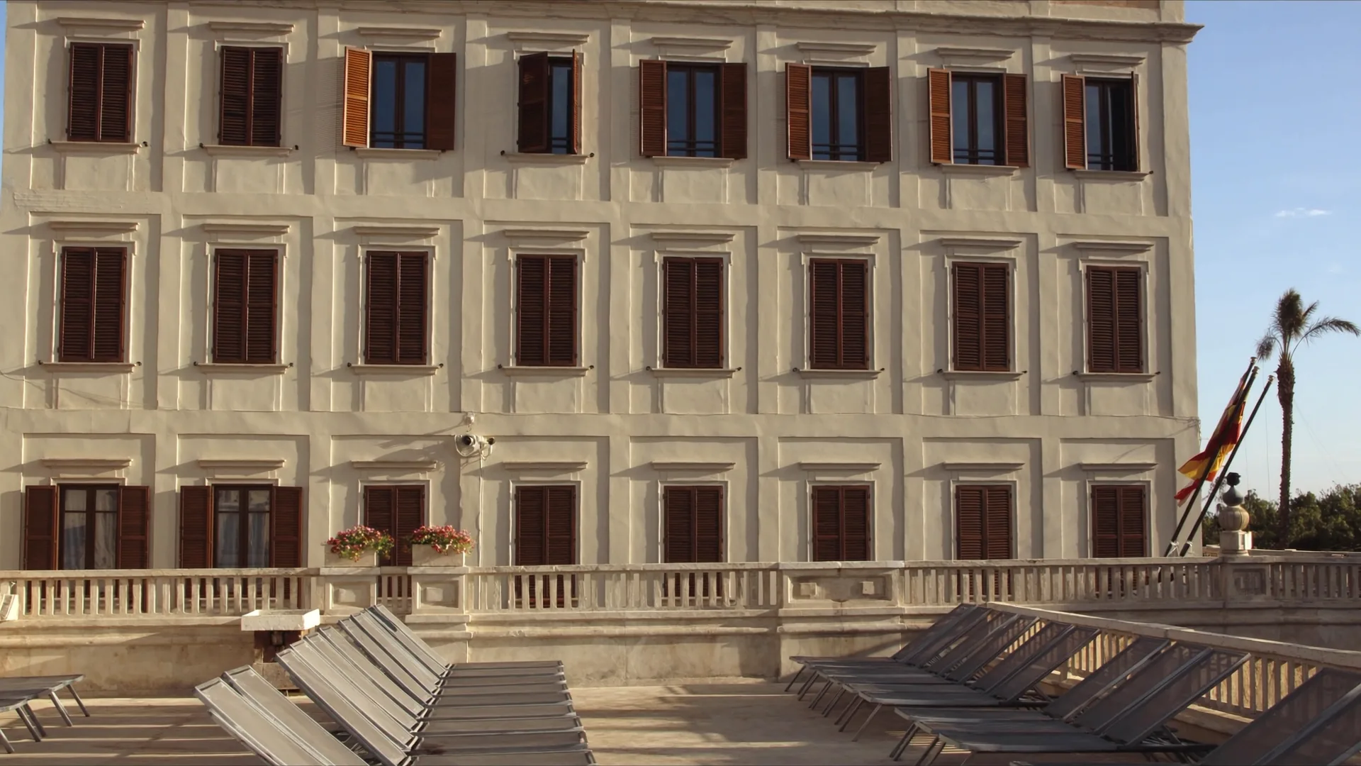 Façade d'hôtel côtier méditerranéen dans la lumière matinale avec transats empilés sur la terrasse, en attente de l'ouverture saisonnière