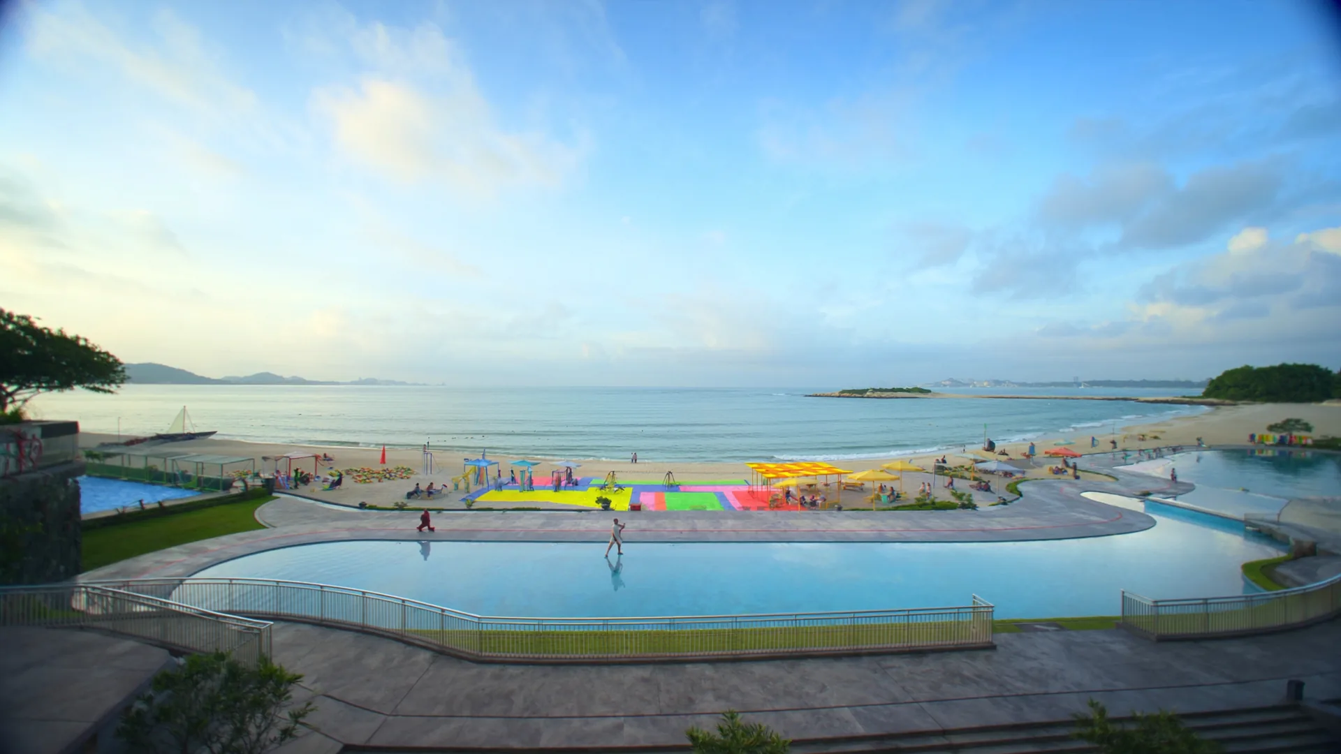 Beachfront family resort at morning light with colourful play structures near the shore and tiered pool areas
