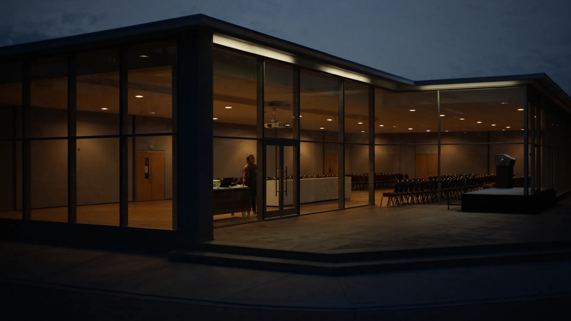 Modern hotel conference wing at dusk with floor-to-ceiling glass revealing an empty ballroom prepared for theatre-style seating